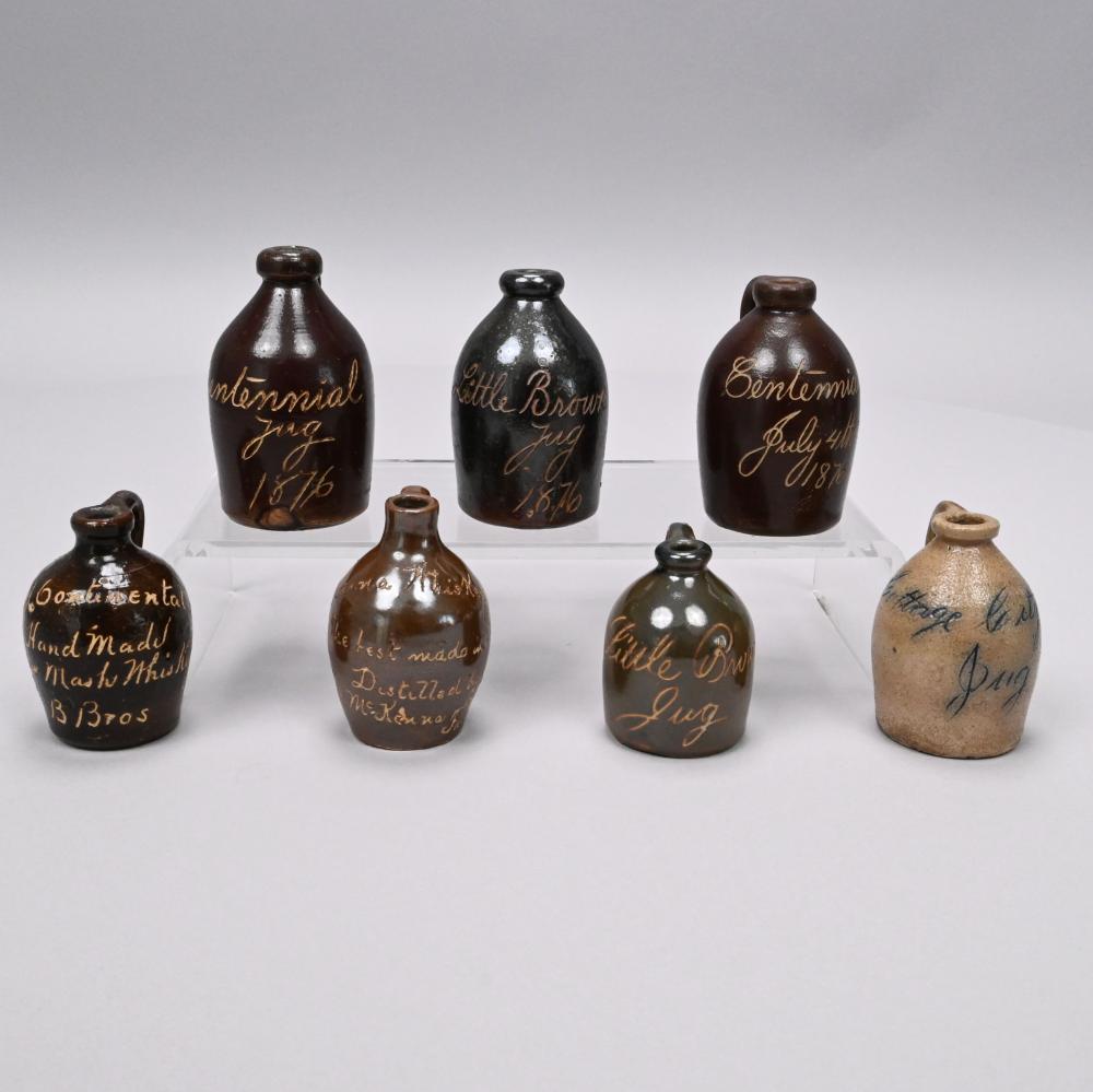 Seven Stoneware Souvenir and Advertising Jugs sold by Devin Moisan Auctioneers, Inc., lot 841 — auction record photograph