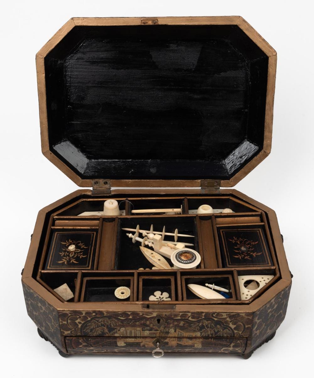 Open rectangular lacquered sewing box with compartments holding bone or ivory-like sewing tools and small accessories, decorated with floral and bird motifs.