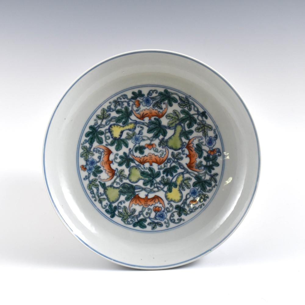 Porcelain decorative plate with blue floral border and multicolored flowers and leafy scrollwork in the center.