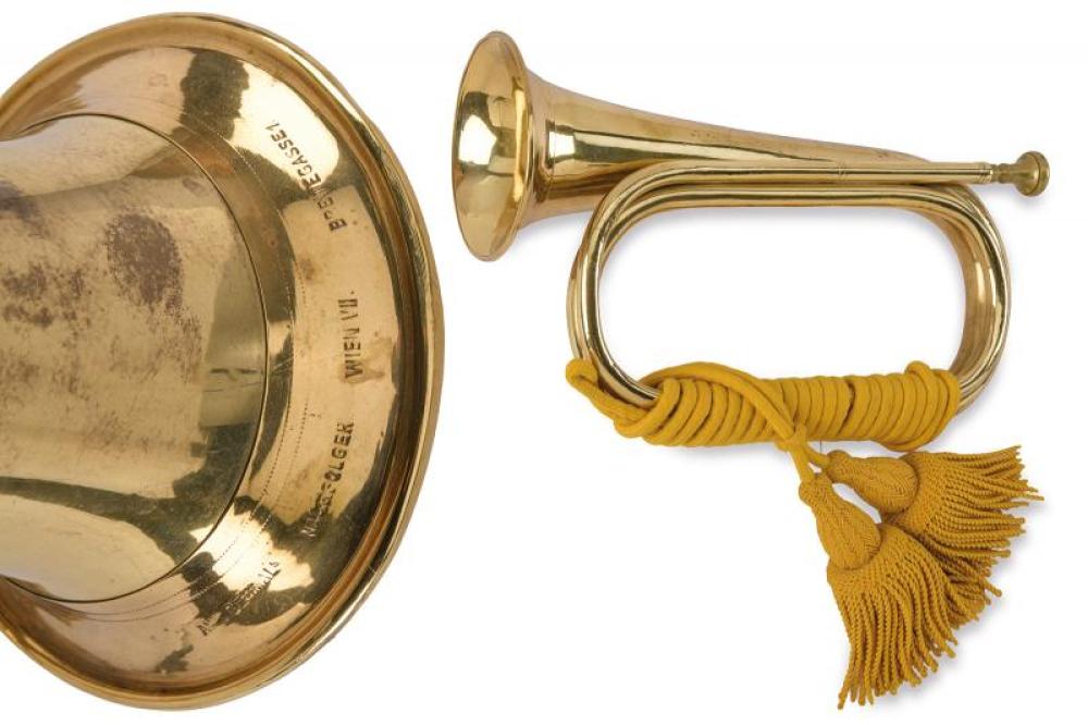 Gold-colored brass trumpet with curved tubing, flared bell, and a yellow braided carrying cord with tassels.