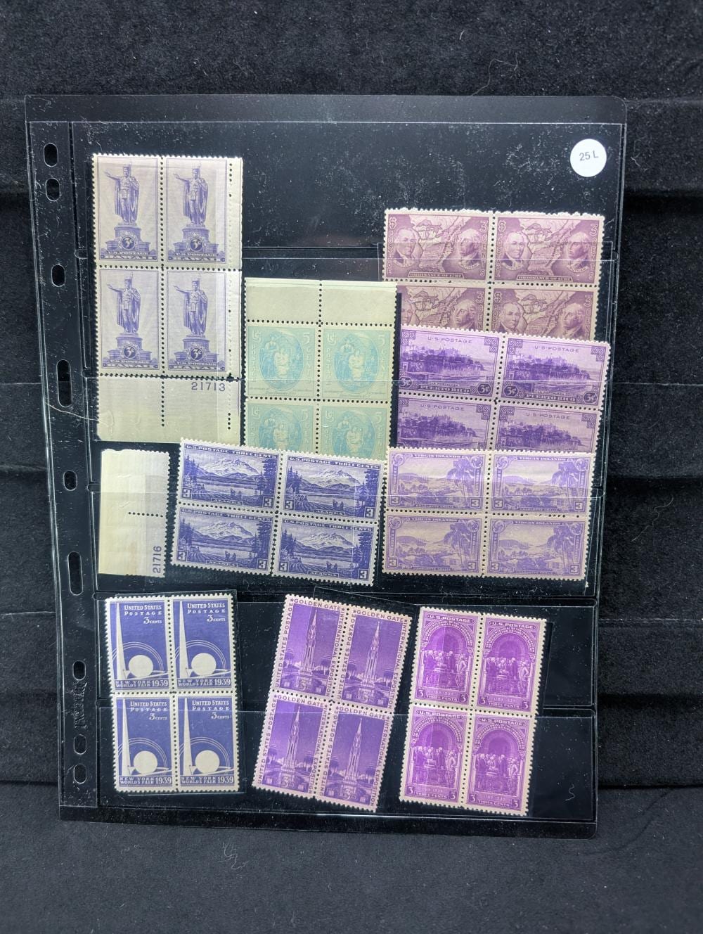 A clear plastic stamp album page holding multiple mint U.S. postage stamps in several colors, including blue and purple blocks.