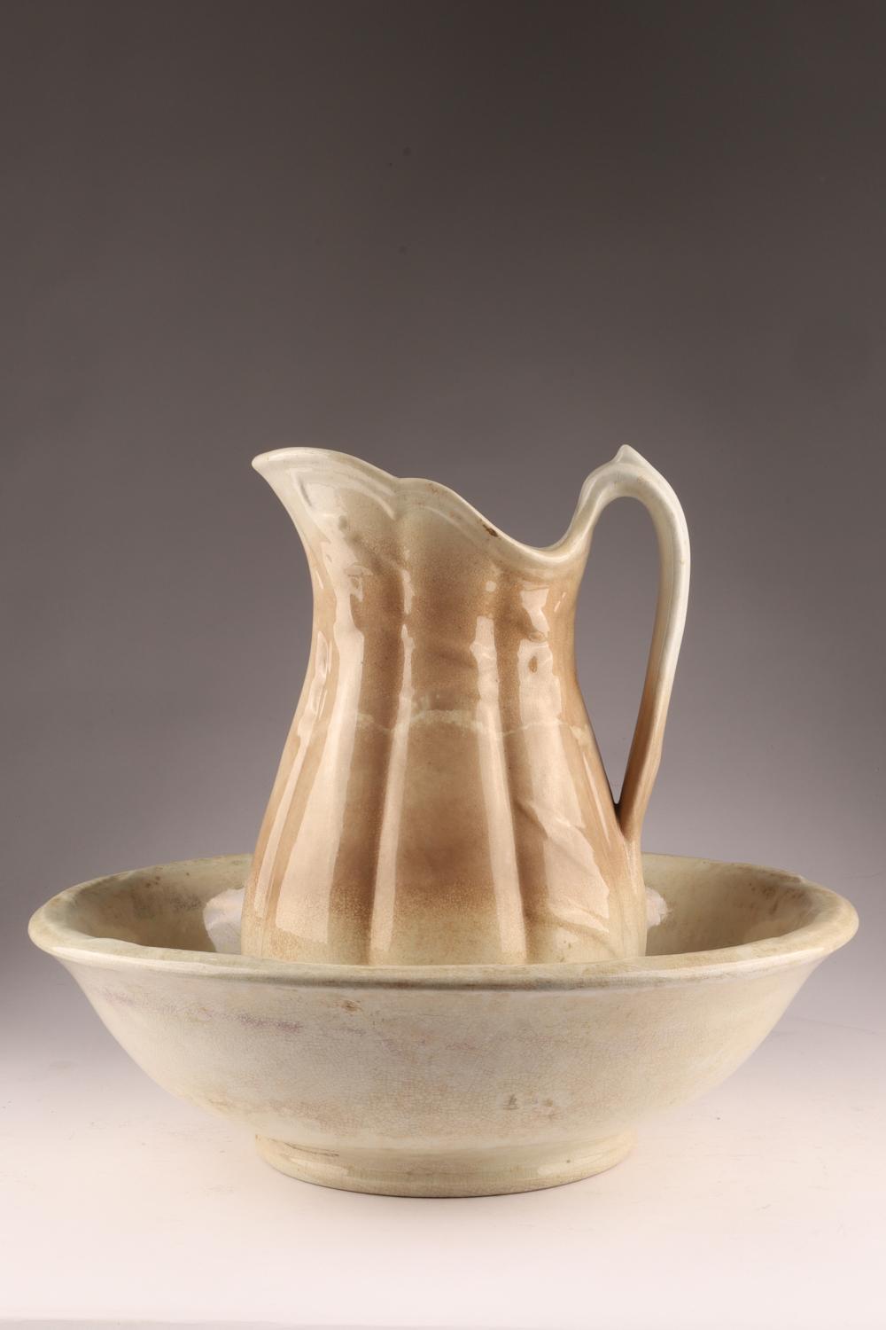 Cream-colored ceramic wash basin with a matching handle pitcher filled to the rim, shown on a gray studio background.