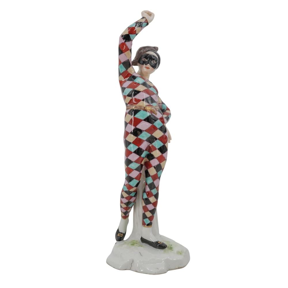 Painted ceramic figurine of a standing clown or commedia-style performer wearing a multicolor diamond checkered outfit and holding one arm up.
