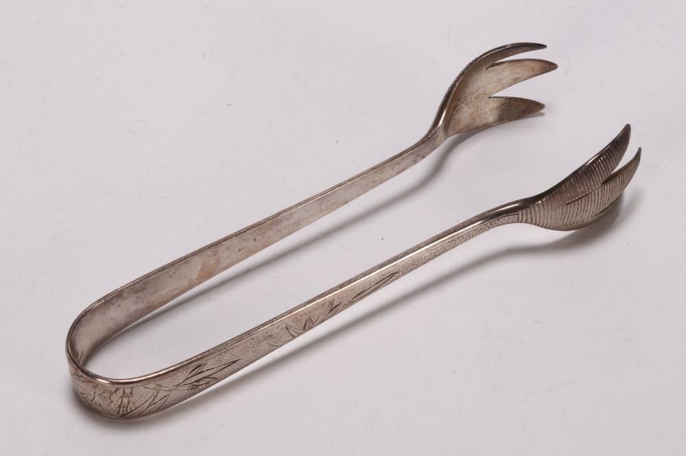 Pair of metal ice tongs with leaf-pattern handles and curved prongs, shown on a white background.