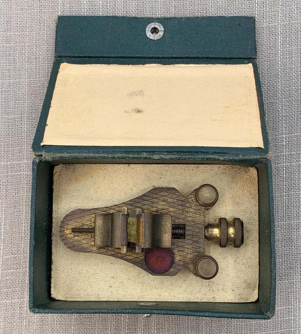 Miniature jeweler or watchmaker poising vise tool displayed inside a dark green hinged case with a beige interior lining.