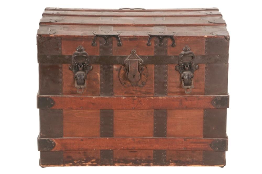 Red-brown banded steamer travel trunk with metal corner guards and central latch hardware, viewed from the front.