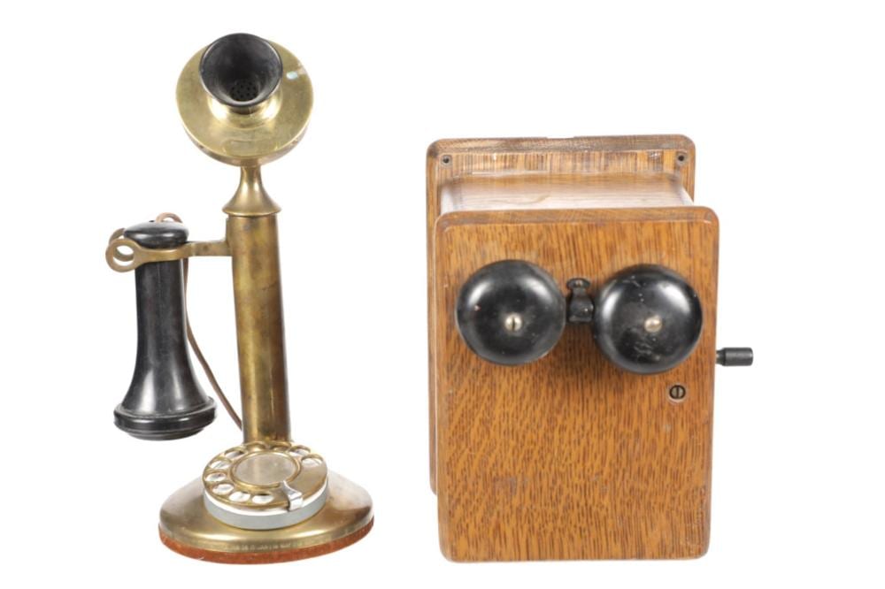 Brass candlestick telephone with a black base and receiver stand, shown with a matching wooden box containing two black handset cords.