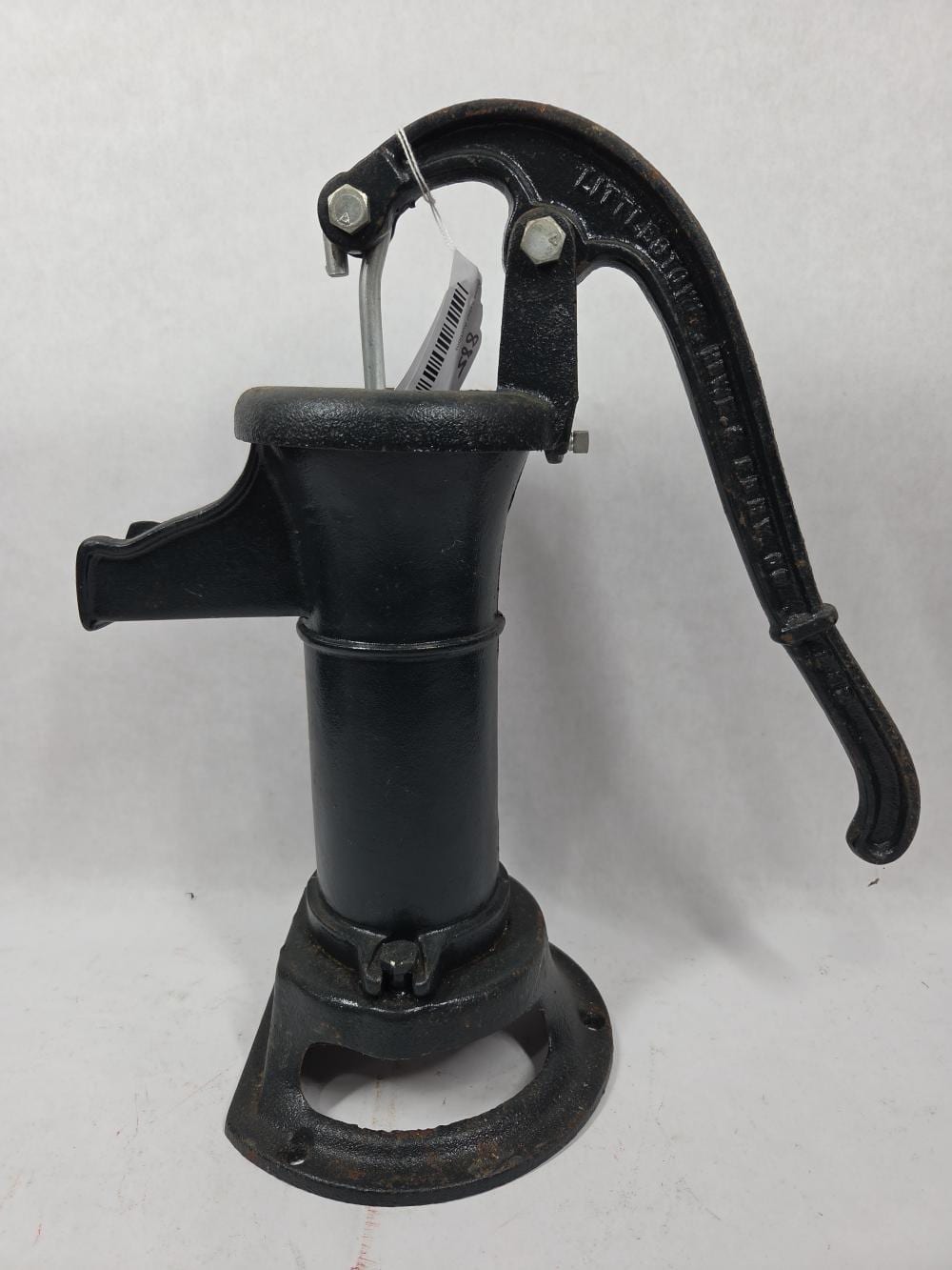 Black cast-iron hand pump with a lever handle and spout on a base.