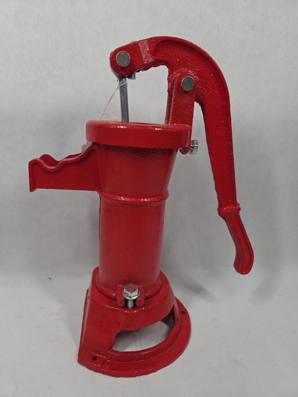 Red manual water pitcher pump with curved spout, lever handle, and metal stem on a round base.