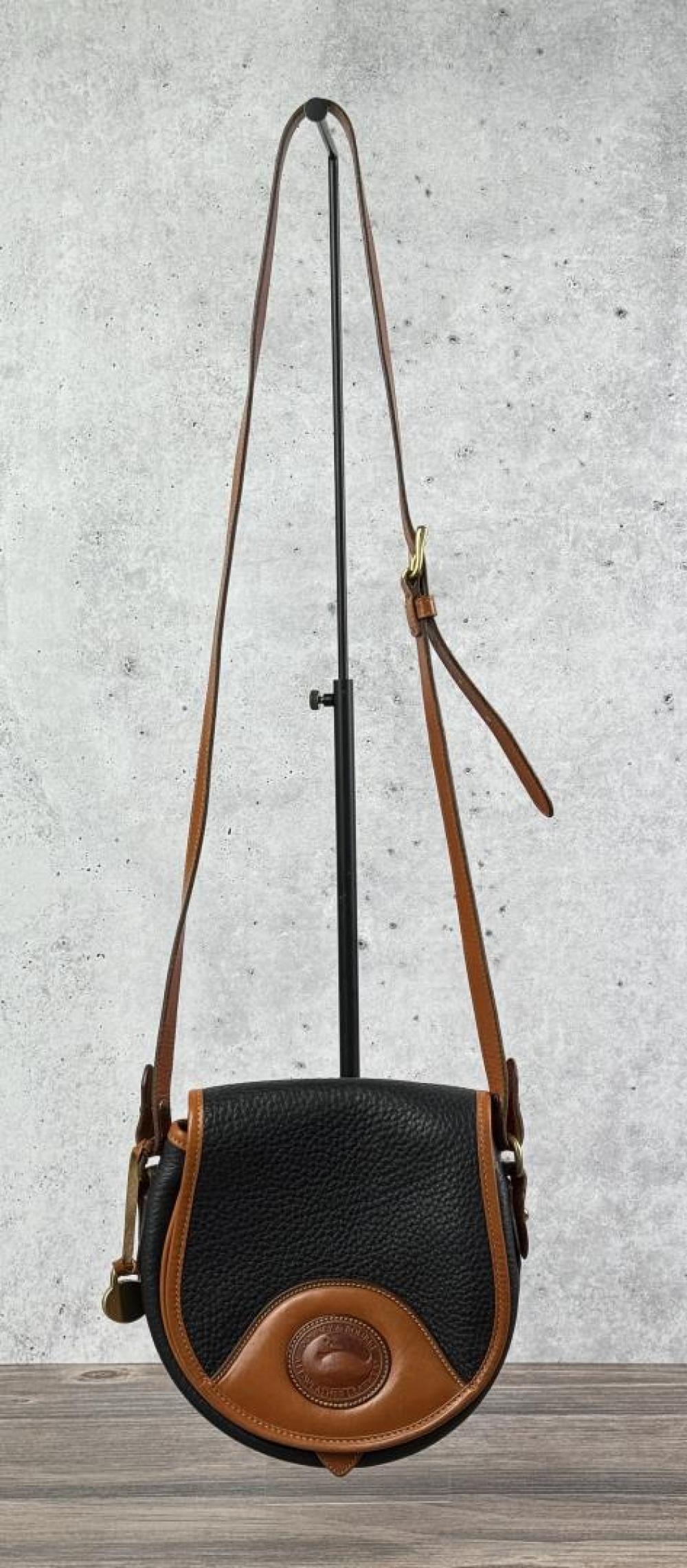 Brown-and-black leather crossbody purse on a stand with a curved front flap and gold clasp.