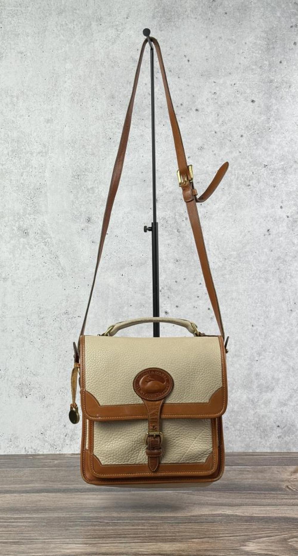 Front view of a small tan and cream leather crossbody/shoulder purse with a flap, front emblem patch, and leather strap.