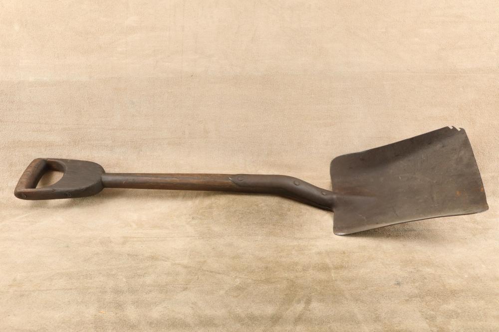 Metal shovel with a dark D-handle and rectangular spade lying horizontally on a neutral background.