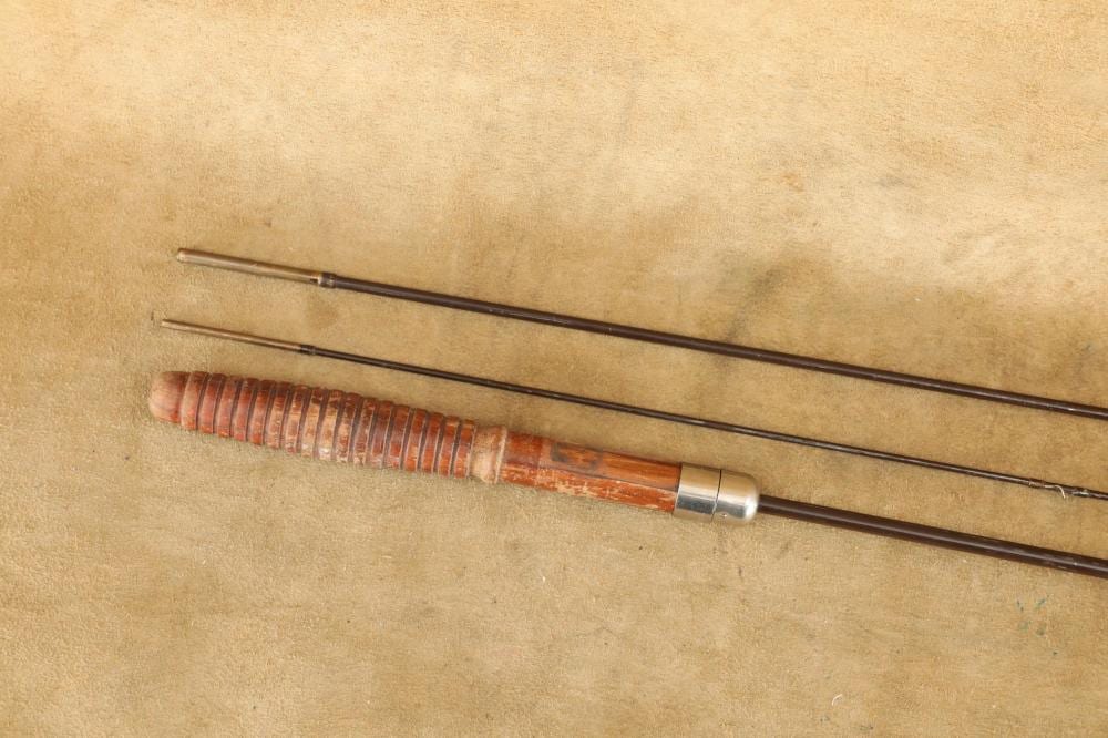 Close-up of a two-piece fishing rod with a brown handle and reel seat, lying on a beige background.