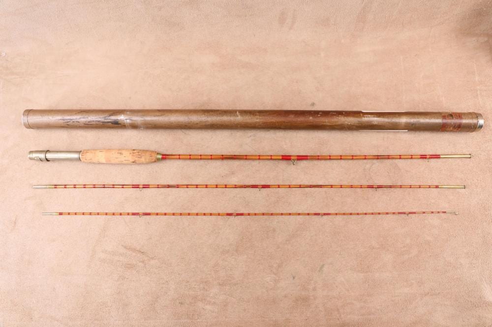 Three-piece vintage bamboo fly fishing rod laid out horizontally with an orange-and-red striped section and reel seat area visible.
