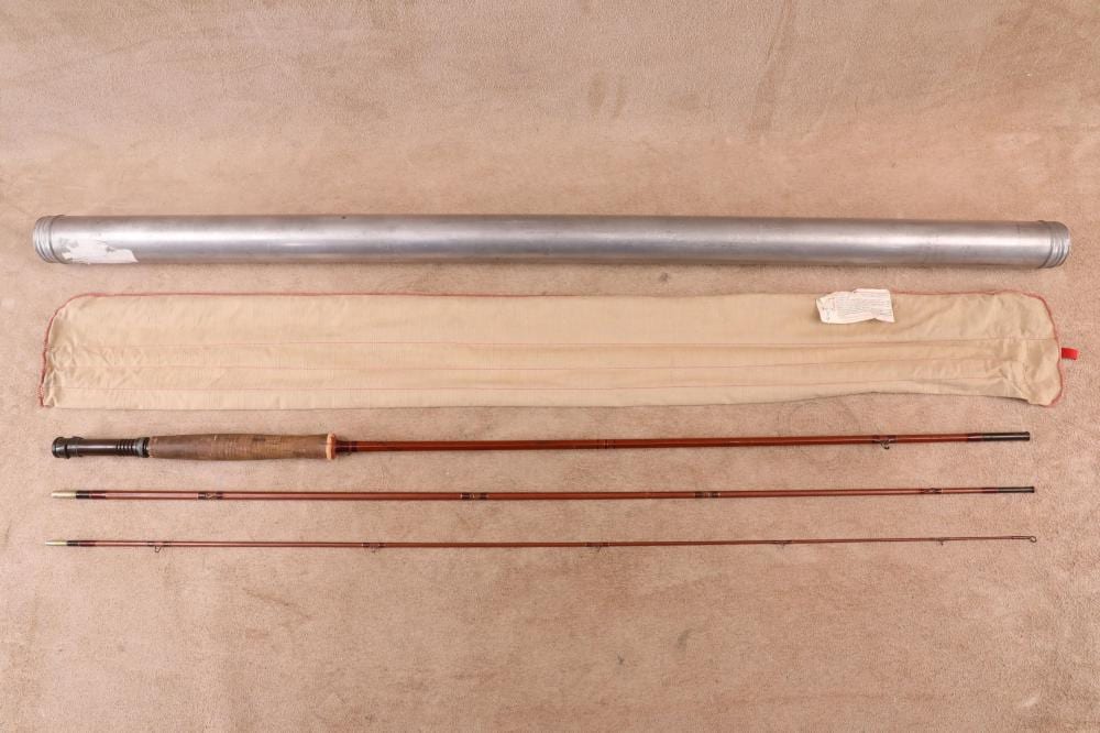 Vintage fishing fly rod with three sections laid out beside a light canvas storage tube on a beige background.