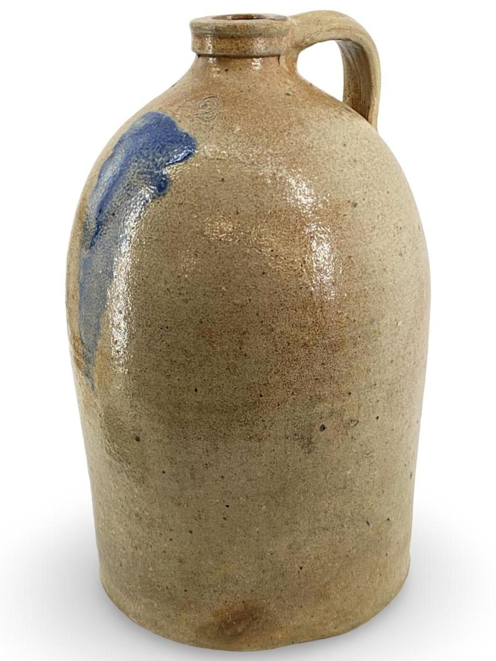 Glazed ceramic stoneware jug with tan body, blue and white glaze decoration, and a curved handle.