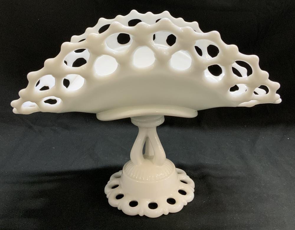 White milk glass pedestal fruit bowl with an openwork lace-like rim and scalloped base on a dark background.