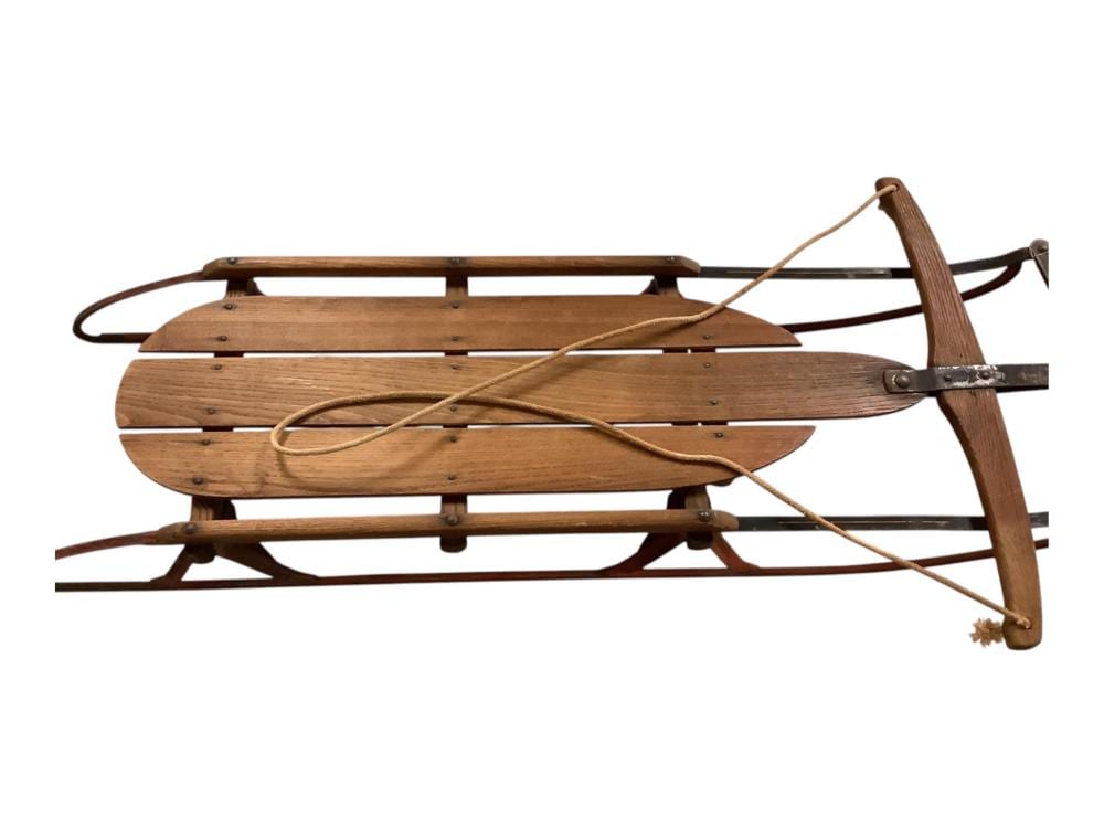 Wooden vintage sled with curved runners, crossbar, and rope tied near the front.