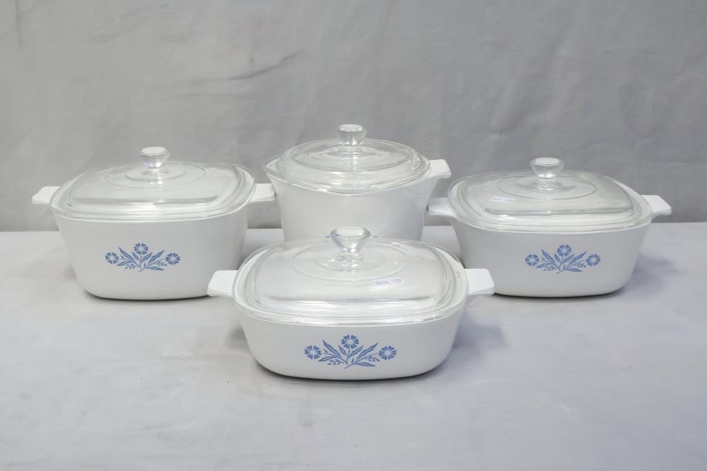 Four white ceramic casserole dishes with blue cornflower pattern and clear glass lids on a tabletop against a light background.