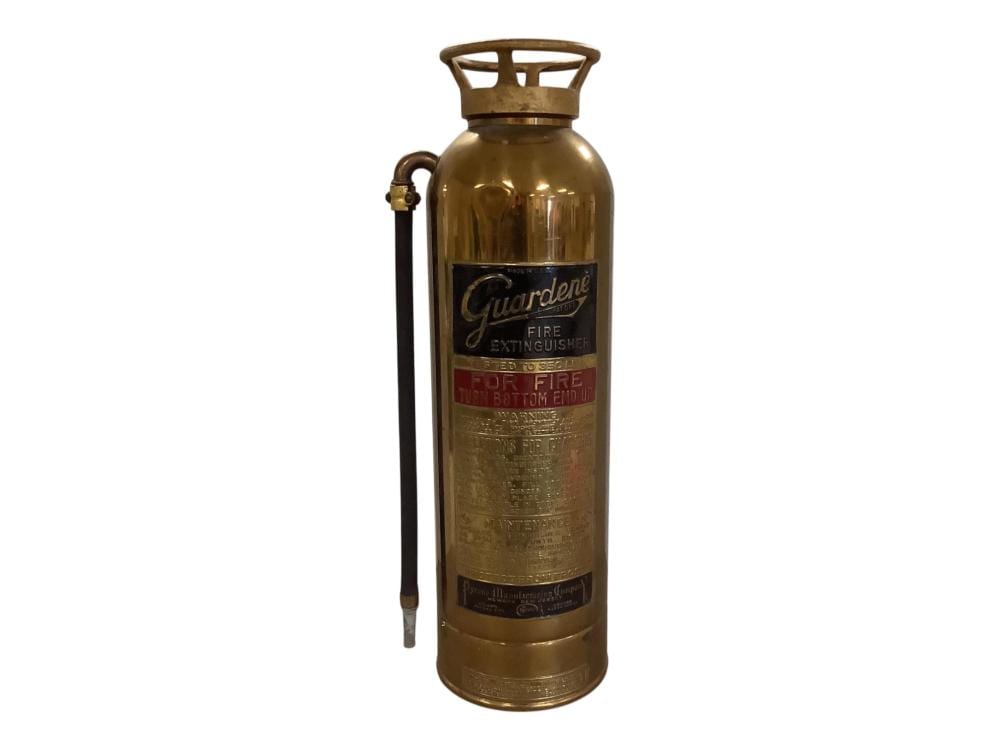 Vintage brass fire extinguisher with a carrying handle and a label reading “Guardene.”