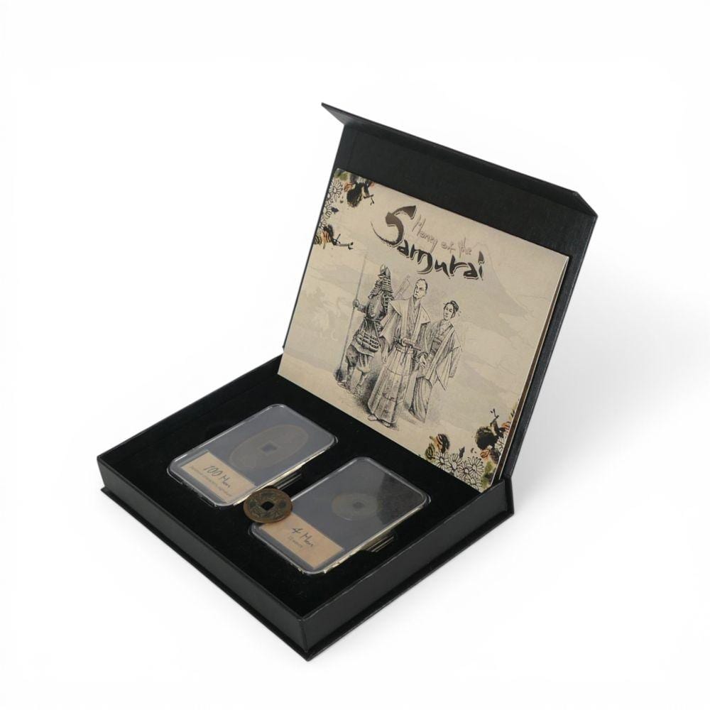 Japanese coins and a banknote displayed in a black presentation box with a printed cover showing samurai figures and decorative flowers.