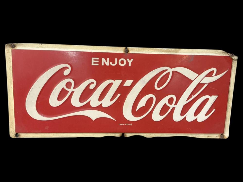 Red metal Coca-Cola sign with white script reading “ENJOY” above “Coca Cola” on a rectangular panel.
