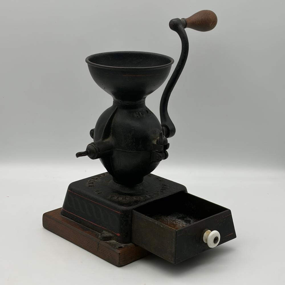 Black cast iron coffee grinder mill with a funnel top and curved crank handle, mounted on a rectangular base with a white knob.