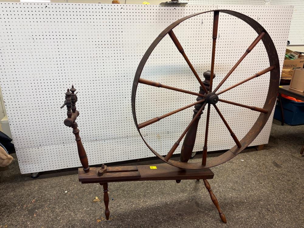Antique wooden spinning wheel with a large circular wheel and spindle on a wooden stand.
