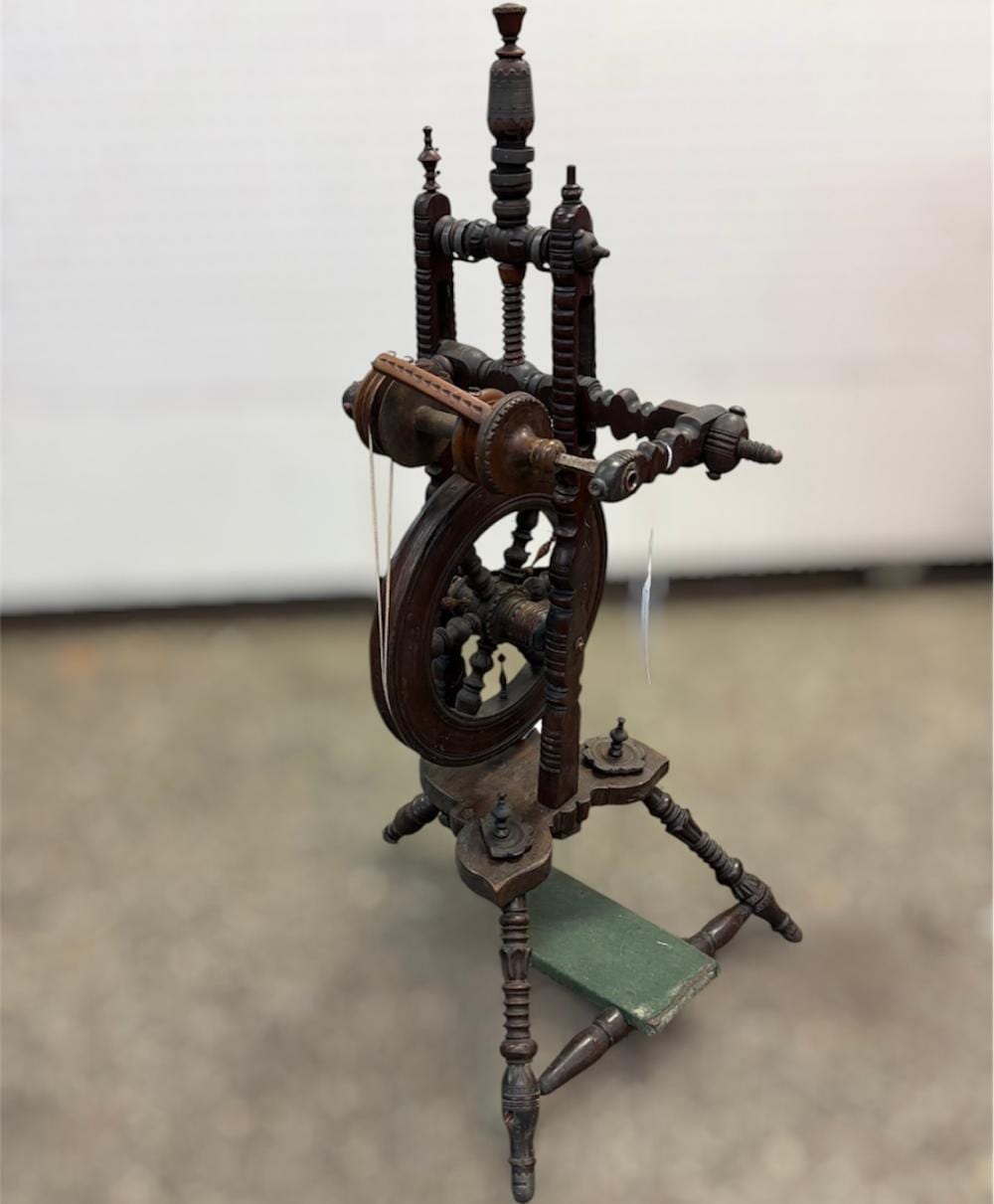 Antique wooden spinning wheel with dark turned posts, a large wheel, and a green base stand, shown in a three-quarter view.