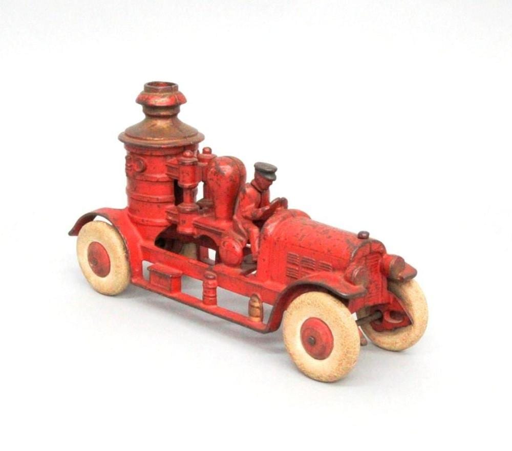 Red cast-iron toy fire truck with rounded cab, raised wheels, and a smokestack, shown on a white background.