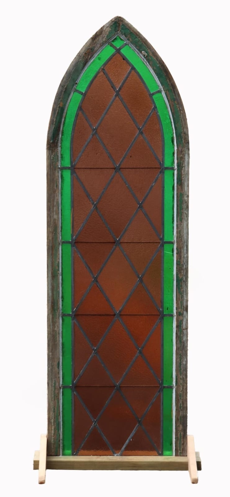 Stained glass window panel with arched top, green borders, and blue diamond lattice over brown glass background.