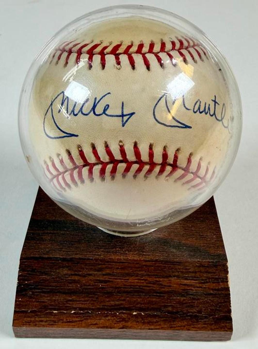 Signed baseball with red stitching, on a dark wooden display stand; blue signature is visible across the ball.
