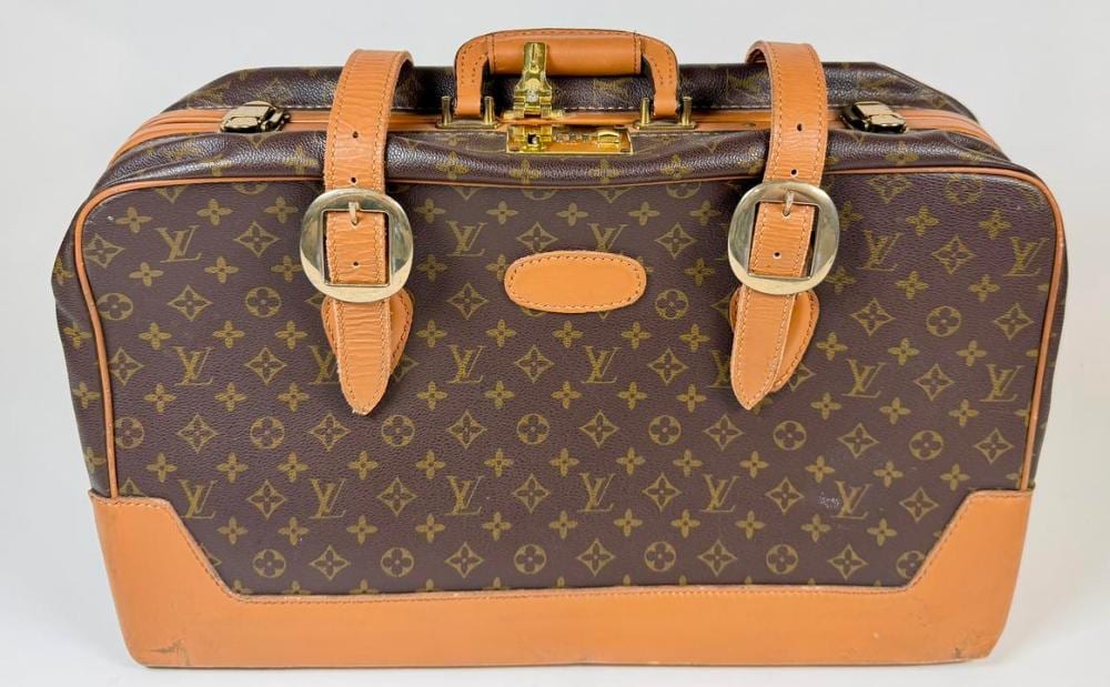 Brown and tan designer-style monogram suitcase with leather handles and metal locks, shown front view.