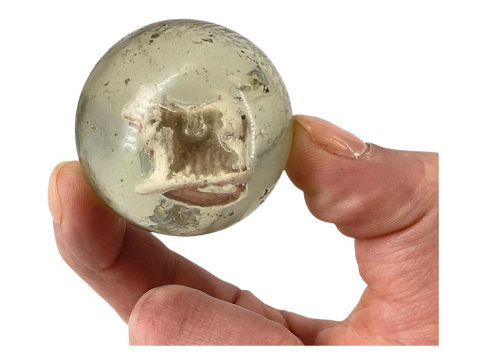 Close-up of a hand holding a round stone sphere with a carved or embedded animal figure in relief.