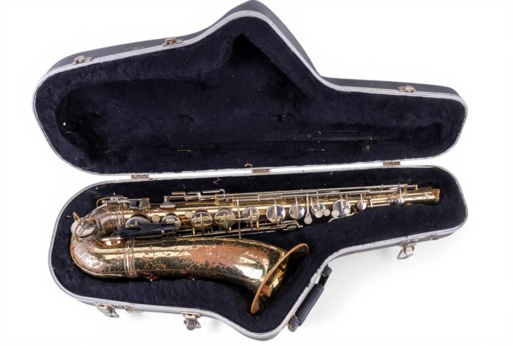 Vintage brass saxophone resting inside an open black case with foam lining against a white background.