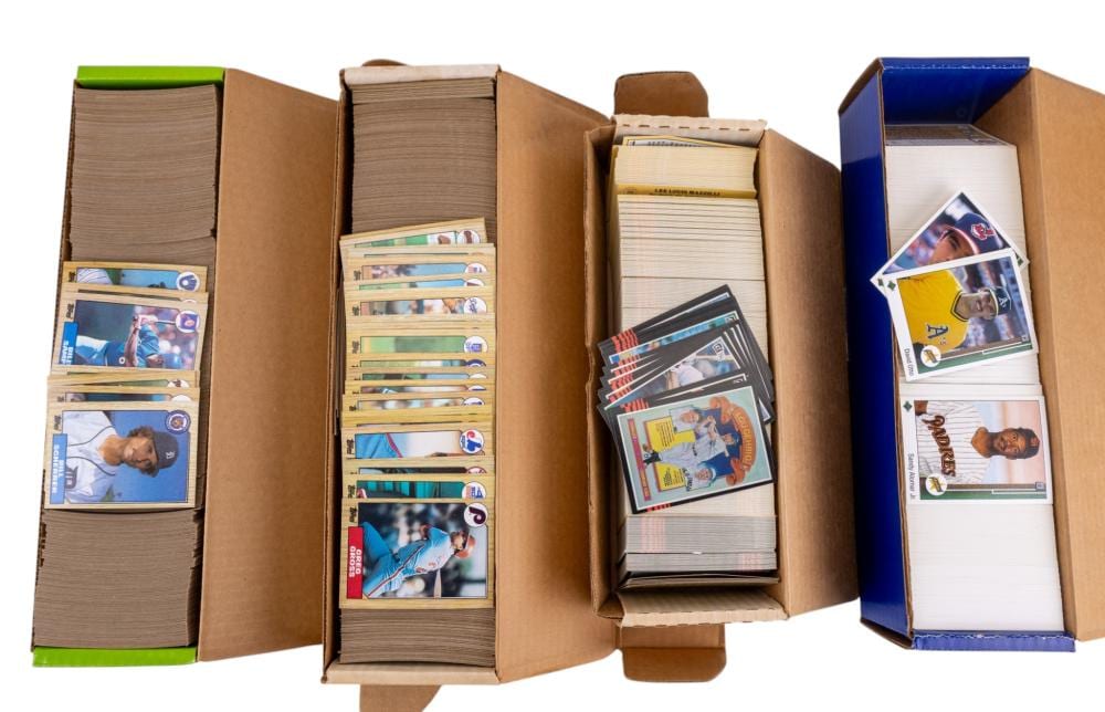 Several stacks of baseball trading cards in open cardboard boxes, including individual cards with players’ photos and team logos.