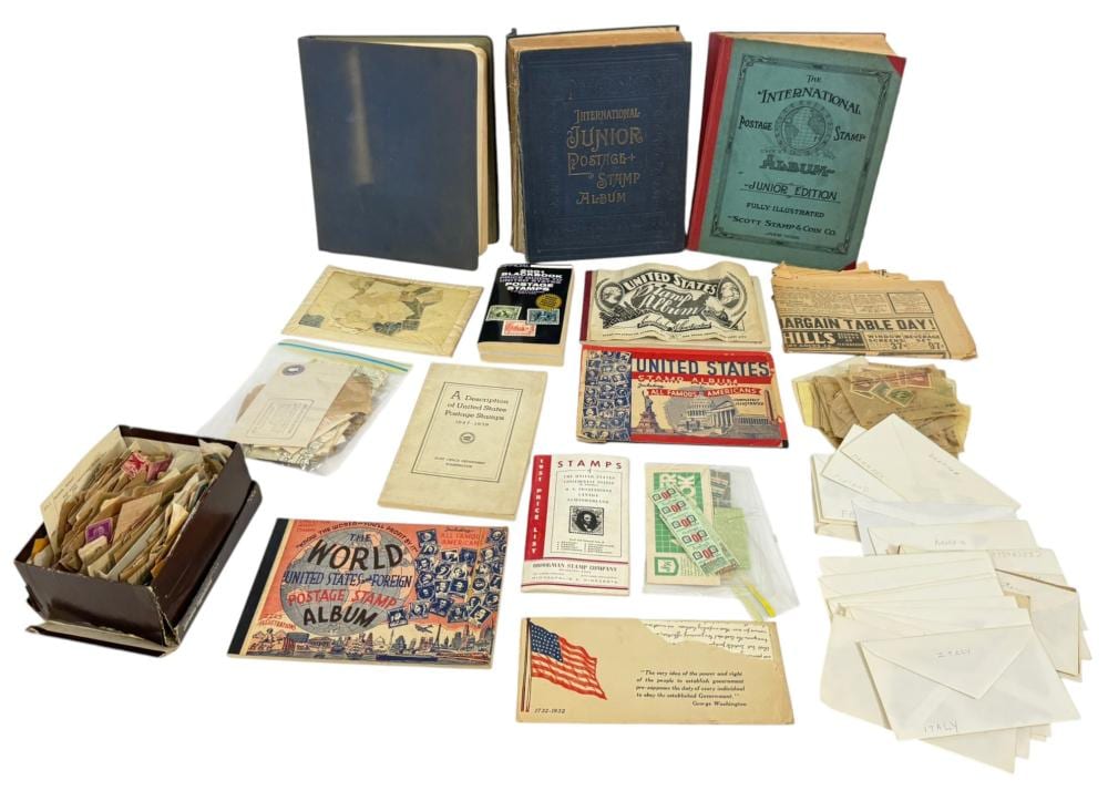 Assorted vintage postage stamp albums and loose stamps in envelopes laid out together on a white background.