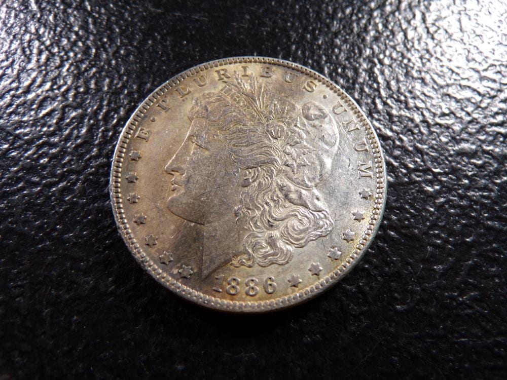 Close-up of a silver coin with Abraham Lincoln’s profile and the date 1886, lying on a dark textured surface.