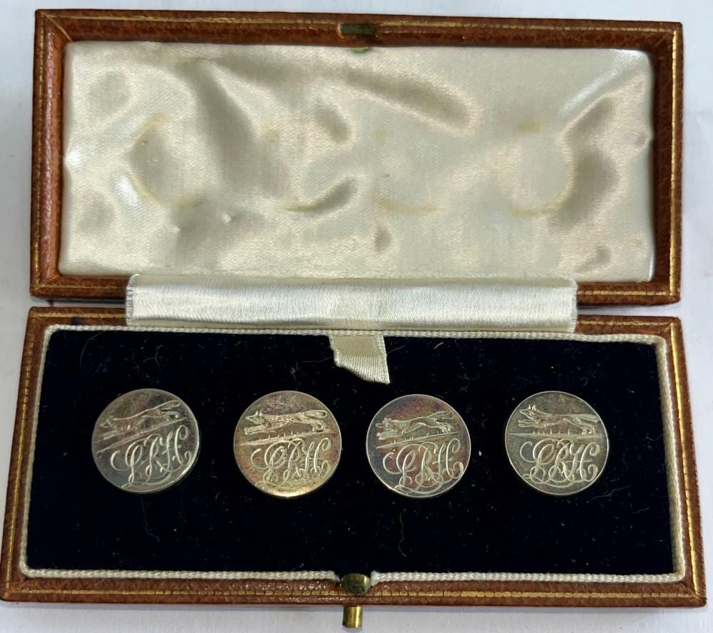 Set of four round silver-toned livery buttons with engraved fox hunting scenes and a monogram, displayed in an open case.