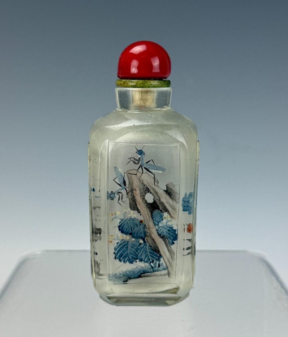Clear glass snuff bottle with a red domed stopper and blue painted figures on the body.