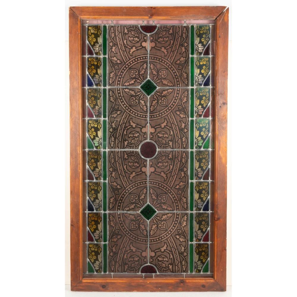 Rectangular stained glass window in a wooden frame with a central circular rosette pattern, colored green diamonds, and vertical bands of floral motifs.
