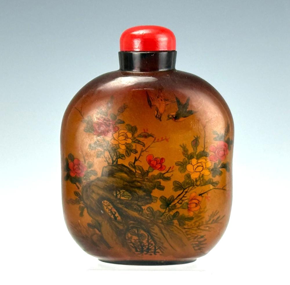 Amber glass snuff bottle with a red cap and painted interior scene of flowers and birds