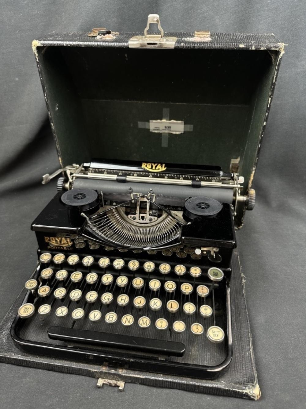 Vintage Royal portable typewriter with round keys and a hard travel case shown open on a dark background.