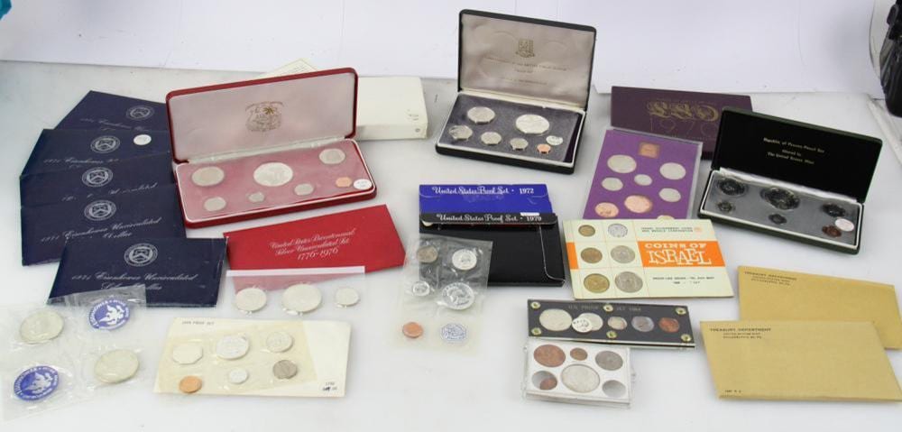 Assorted coin proof sets and individual coins laid out in presentation cases and sleeves on a table.