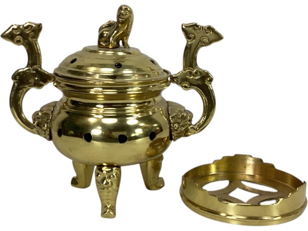 Gold-colored brass incense burner shaped like a three-footed vessel with three animal-like handles and a perforated lid with a standing figure.