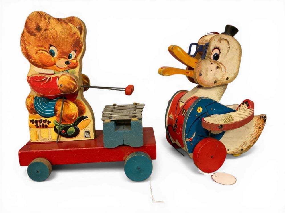Two vintage wind-up style toy figures shaped like animals pulling small carts, one bear with a hammer drum and one dog playing a horn-like instrument.