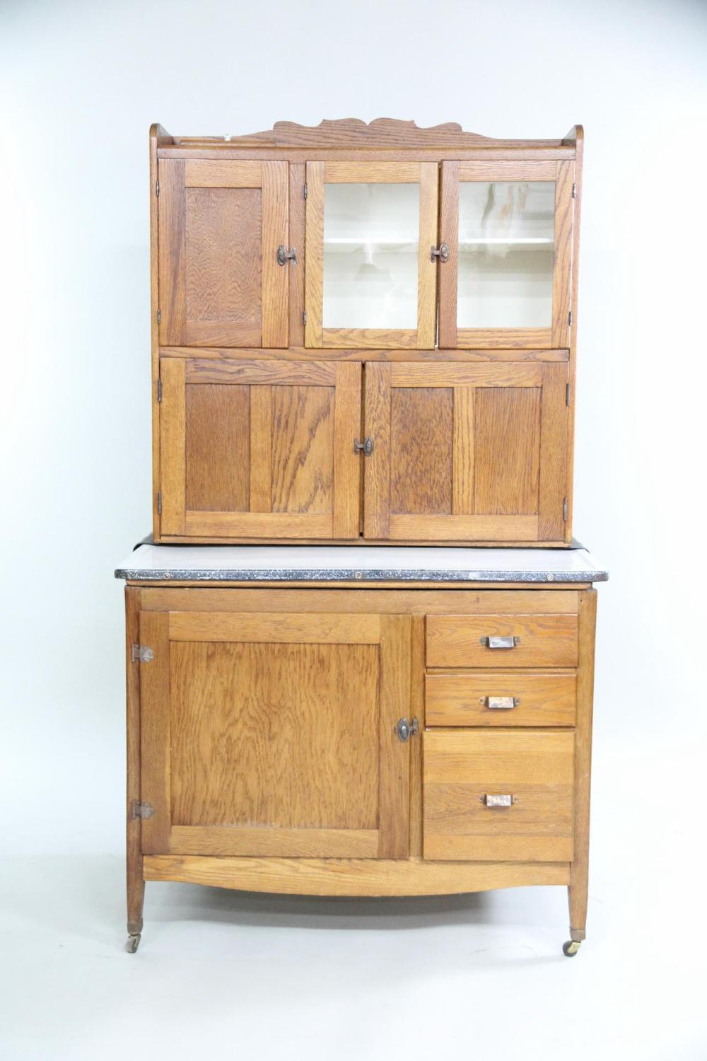Wood cabinet with glass-paneled doors above and multiple drawers and a door below, on turned legs and a gray top edge.