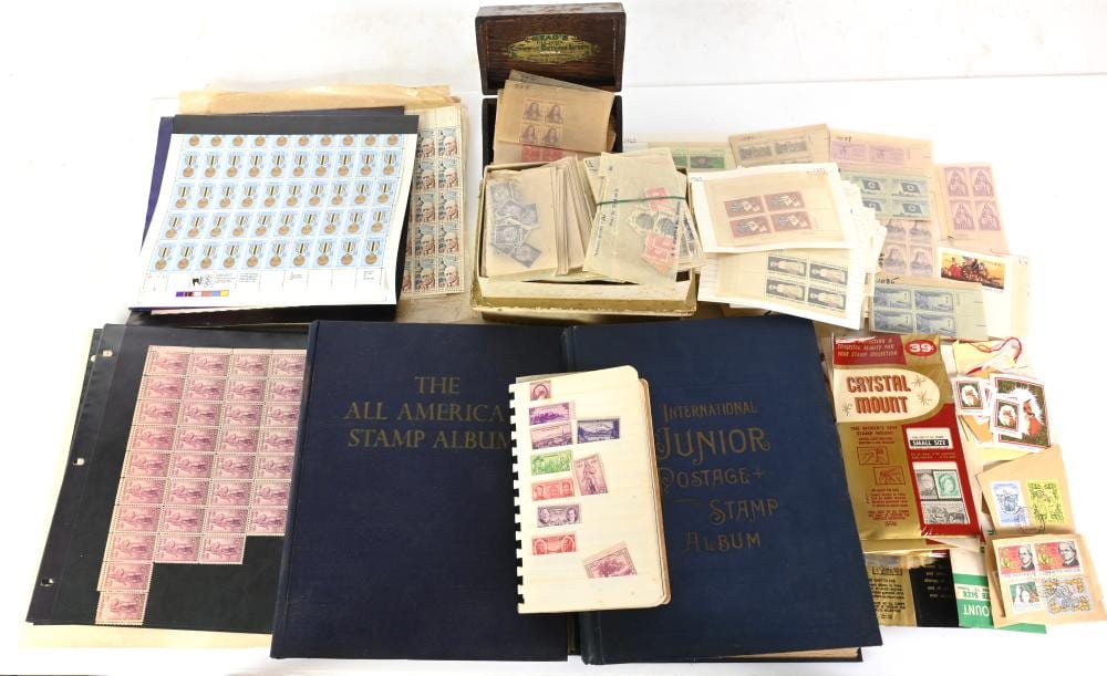 Assorted postage stamp albums and loose stamp sheets, including blue stamp albums and small collections arranged on a white background.