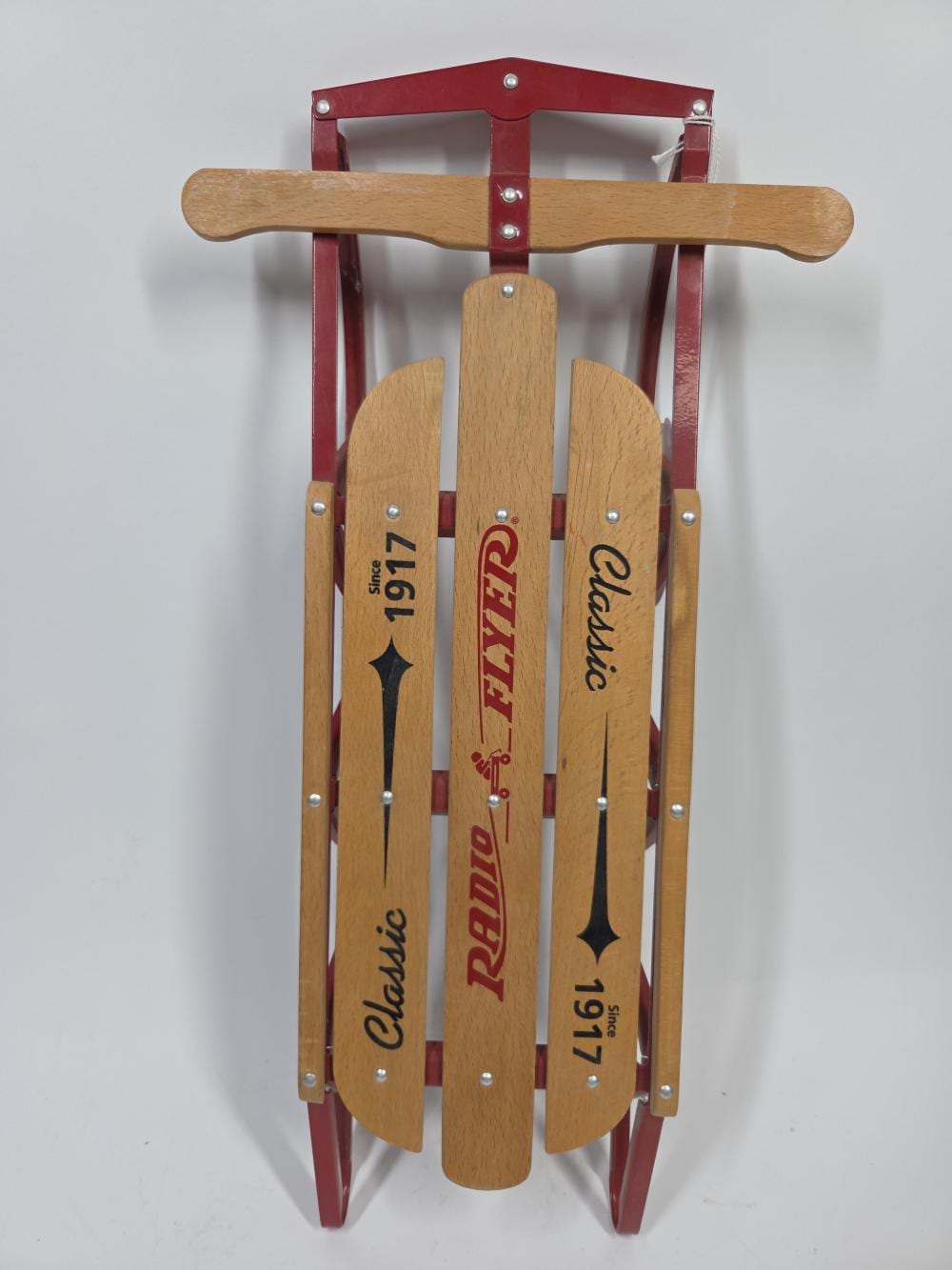 Wooden miniature sled with red metal runners, a wooden handle bar, and printed labels on the side runners.