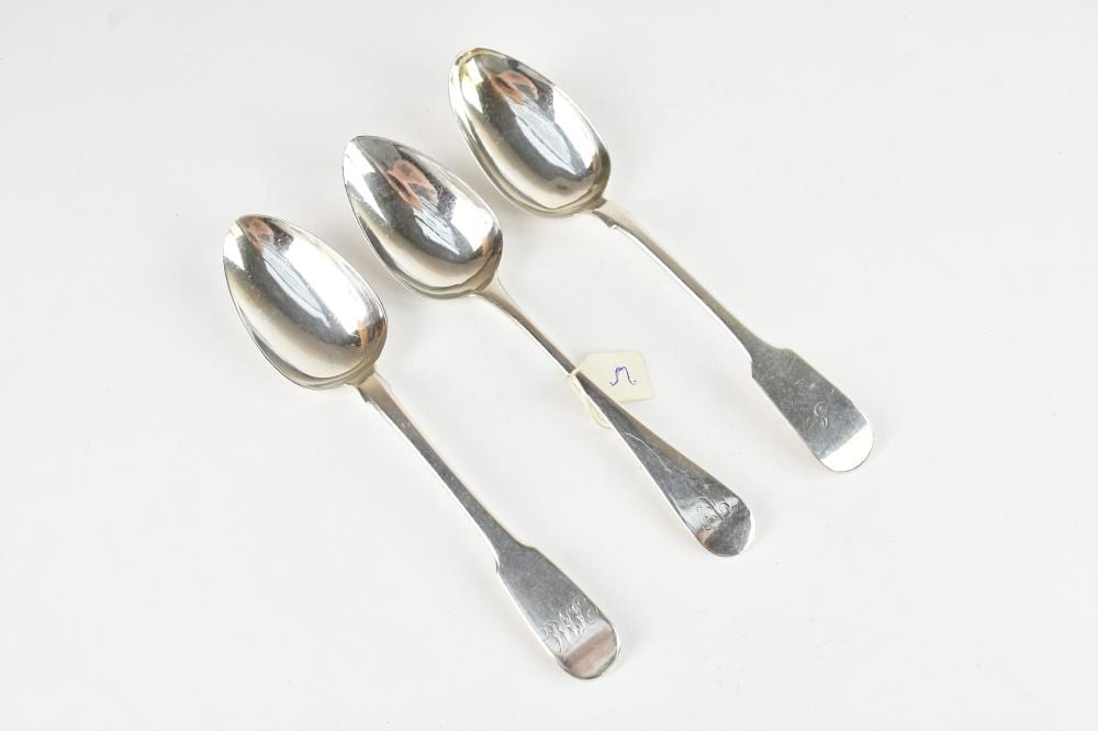 Set of three silver metal teaspoons with oval bowls and engraved handles on a white background.